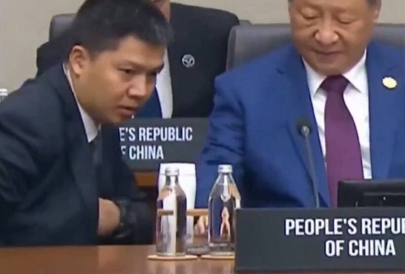 镜头捕捉到，与会的中国国家主席习近平在会议期间入座时，贴身随扈立刻俯身上前，递上三件物品的画面。（取自X）